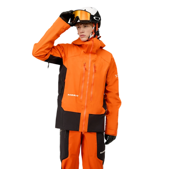 Full body studio shot of man in orange and black Mammut ski suit
