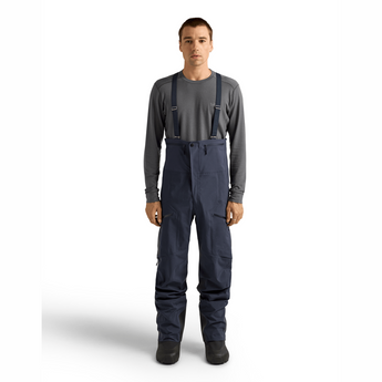 Front view of men's Arcteryx Rush navy bib ski pants with grey long-sleeve shirt